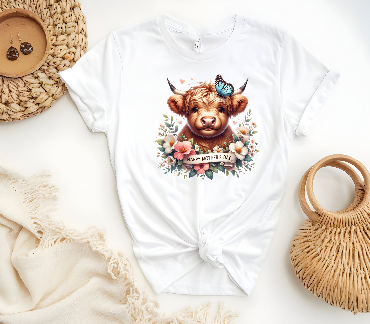 Mother’s Day Inspired Woman’s T-Shirt, featuring a Highland Cow surrounded by beautiful flowers a butterfly and a “Happy Mother’s Day” message.