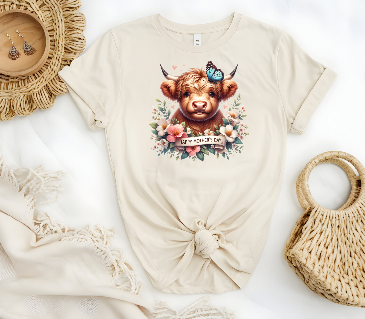 Mother’s Day Inspired Woman’s T-Shirt, featuring a Highland Cow surrounded by beautiful flowers a butterfly and a “Happy Mother’s Day” message.