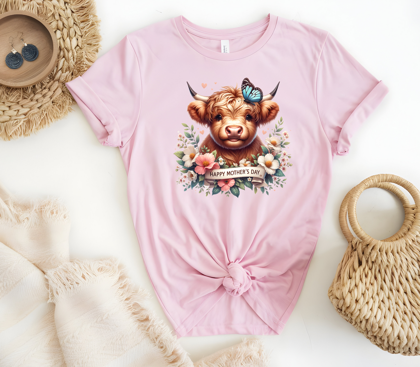 Mother’s Day Inspired Woman’s T-Shirt, featuring a Highland Cow surrounded by beautiful flowers a butterfly and a “Happy Mother’s Day” message.