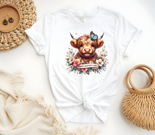 Mother’s Day Inspired Woman’s T-Shirt, featuring a Highland Cow surrounded by beautiful flowers a butterfly and a “Happy Mother’s Day” message.
