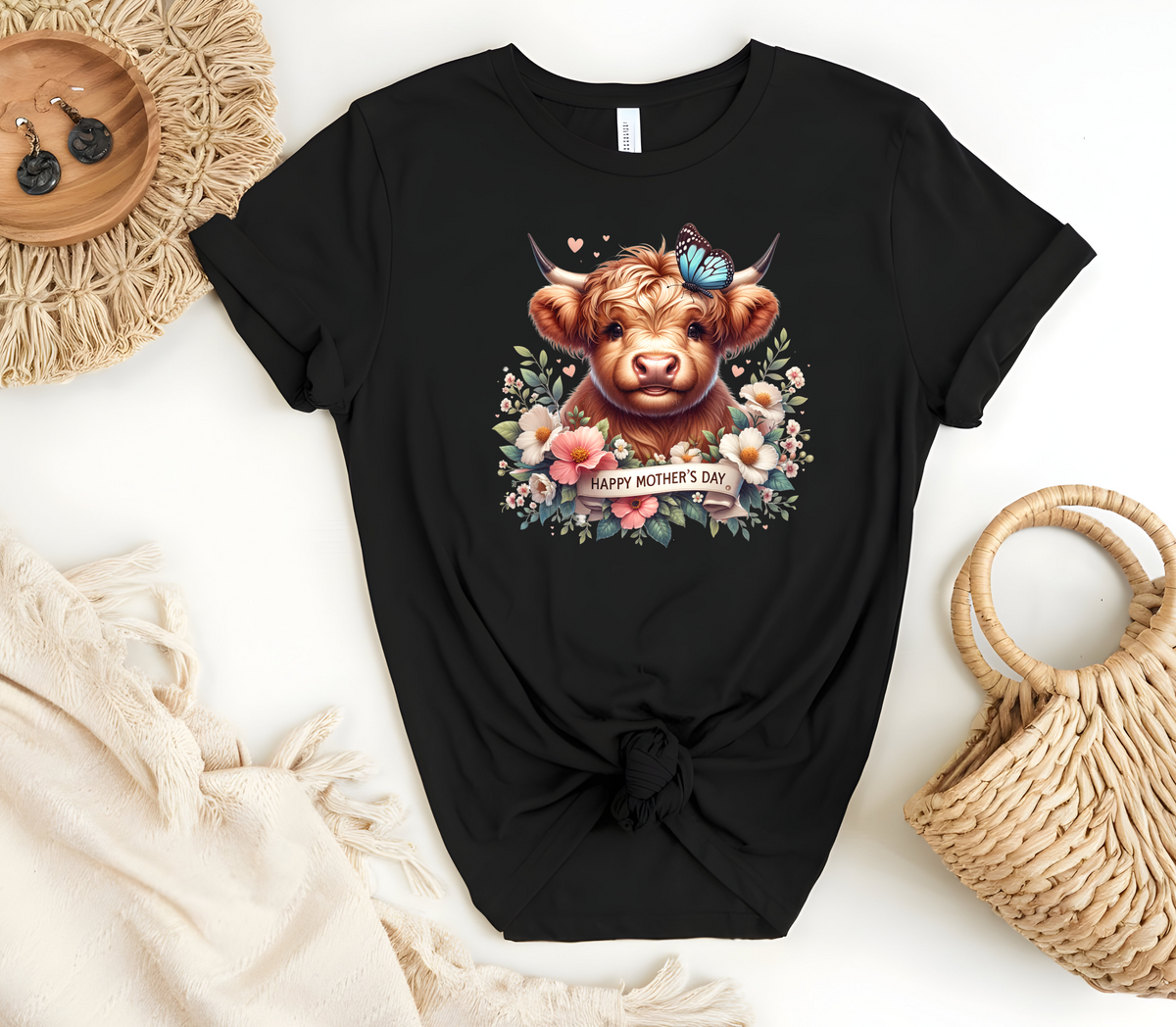 Mother’s Day Inspired Woman’s T-Shirt, featuring a Highland Cow surrounded by beautiful flowers a butterfly and a “Happy Mother’s Day” message.