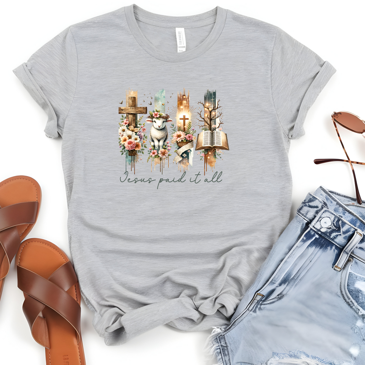 Faith Based Woman’s T-Shirt, featuring beautiful graphic design of a cross, bible, and a lamb with a crown of flowers with the message Jesus Paid It All”.