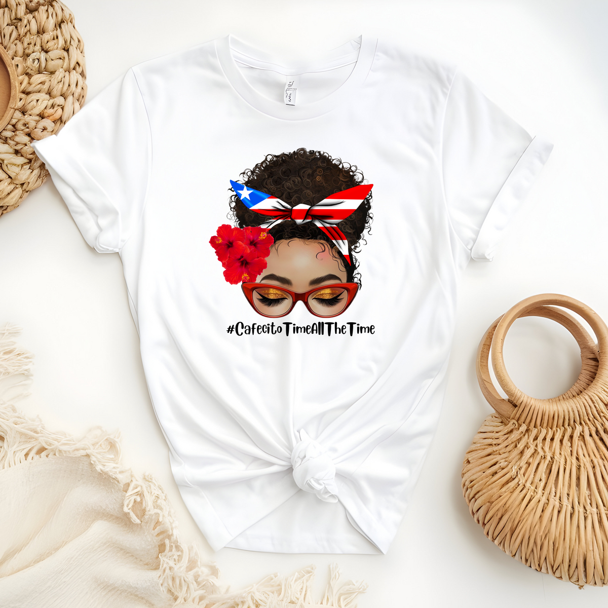 Latina Inspired Woman’s T-Shirt featuring “An Afro Latina messy bun face with curly hair wearing a Puerto Rican inspired Headband, Hibiscus Flowers on her right ear and Red cat eye glasses” with the hash tag “Cafecito Time All The Time”.