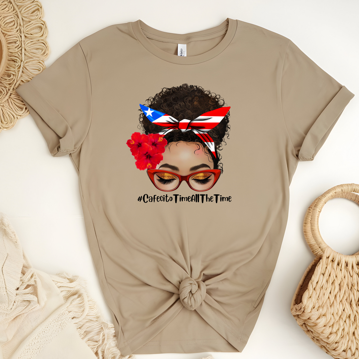 Latina Inspired Woman’s T-Shirt featuring “An Afro Latina messy bun face with curly hair wearing a Puerto Rican inspired Headband, Hibiscus Flowers on her right ear and Red cat eye glasses” with the hash tag “Cafecito Time All The Time”.