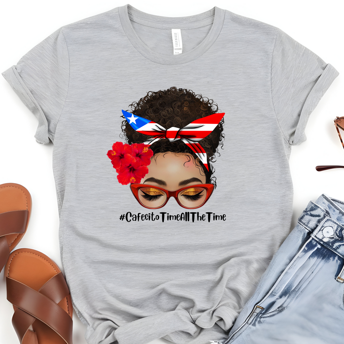 Latina Inspired Woman’s T-Shirt featuring “An Afro Latina messy bun face with curly hair wearing a Puerto Rican inspired Headband, Hibiscus Flowers on her right ear and Red cat eye glasses” with the hash tag “Cafecito Time All The Time”.